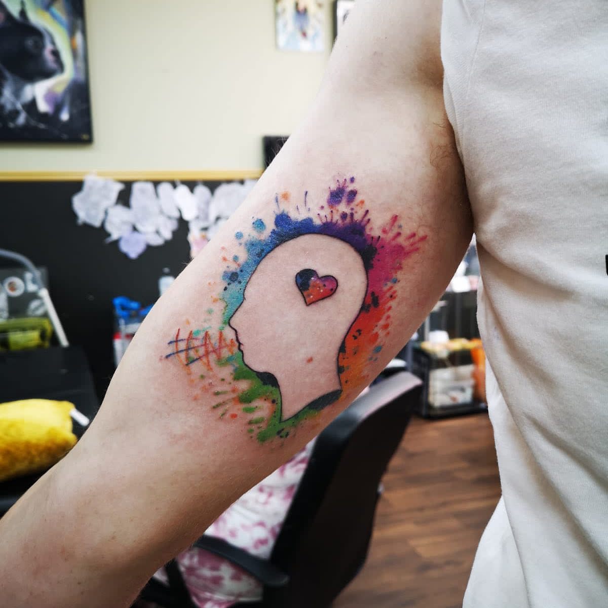 Colorful tattoo of a silhouette with a heart on the arm surrounded by splashes of paint